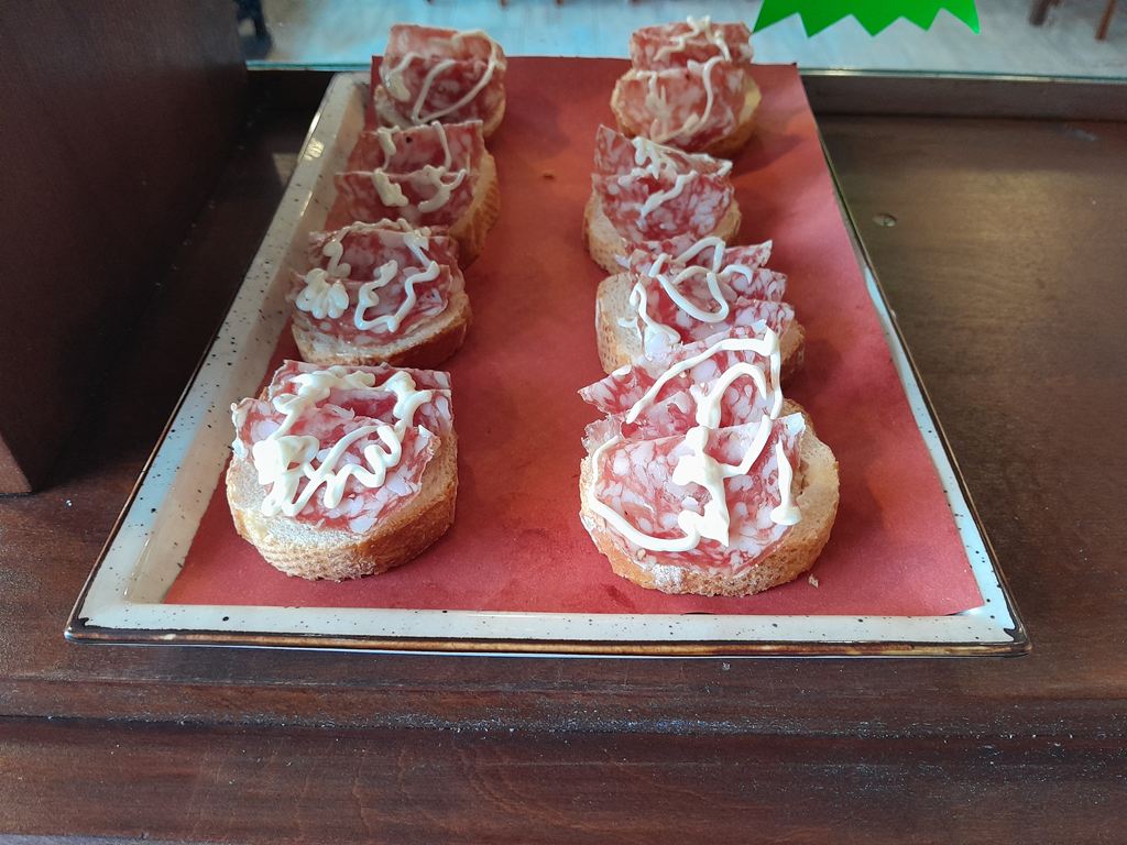 Vassoio di tartine al salame con un filo di maionese appoggiato sul bancone in legno