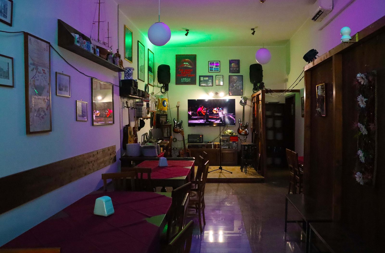 La sala del buffet la sera, con luci verdi e viola, lampade a sfera e in fondo il palco con il televisore acceso